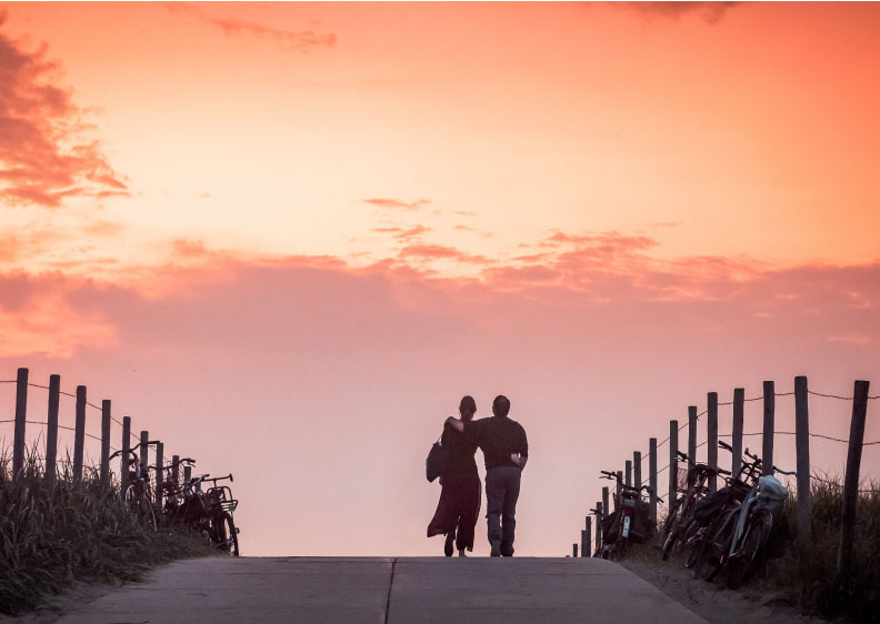 A man and woman walking down a sunset road with an arm around one another