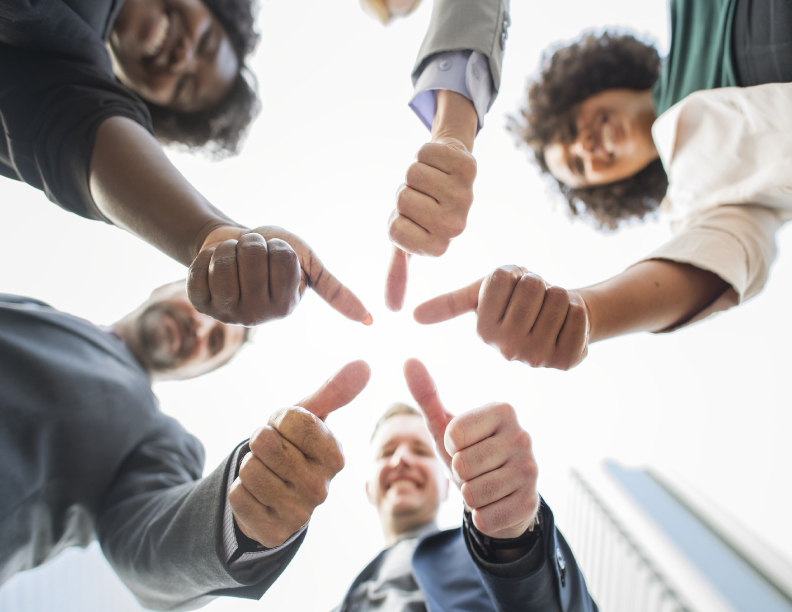 A group of people in a circle with hands extended giving a thumbs up gesture