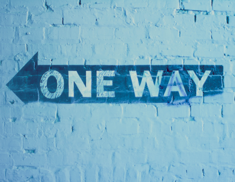 A one way street arrow painted onto a white brick wall.