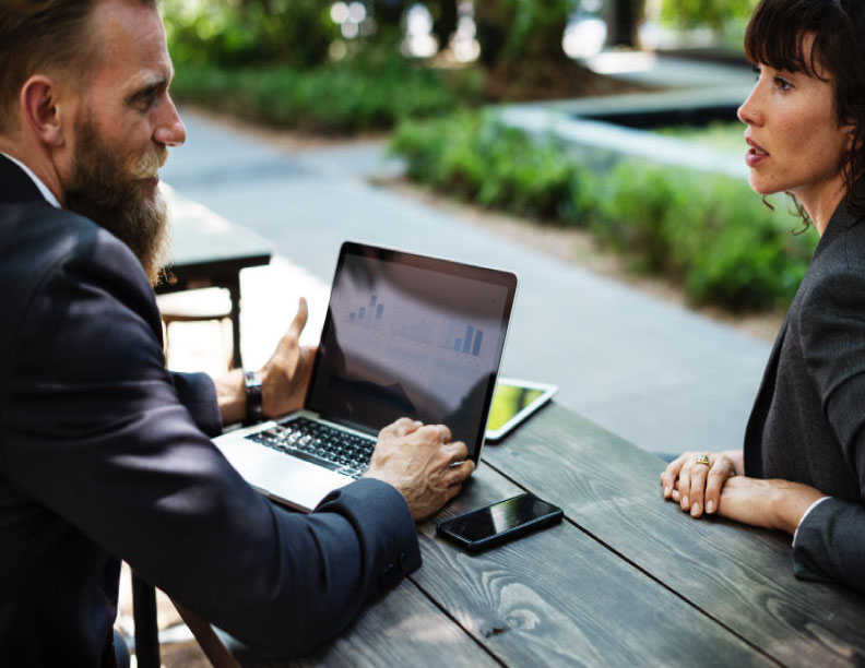 Businessman discussing charts on his laptop with businesswoman at a picnic table